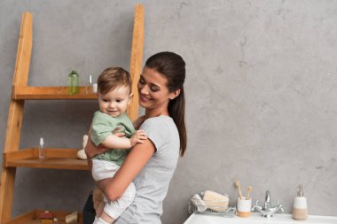 Gülümseyen anne banyoda mutlu çocuğu tutuyor. 