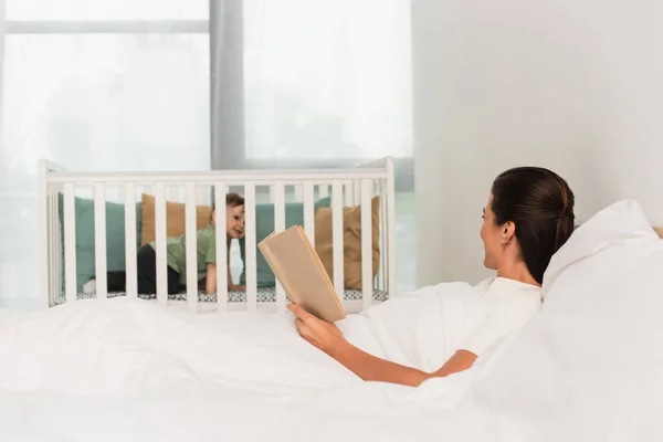 Mujer Con Libro Tumbado Cama Cerca Del Niño Cama Bebé —  Fotos de Stock