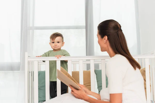 Niño Pie Cama Bebé Cerca Madre Borrosa Con Libro —  Fotos de Stock