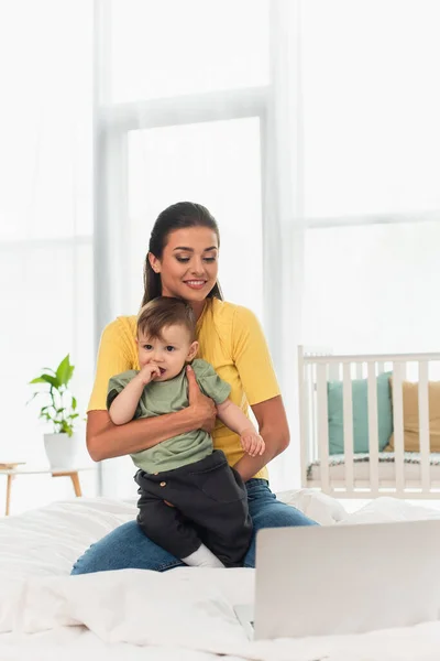 Jonge Moeder Houdt Zoon Buurt Wazig Laptop Bed — Stockfoto