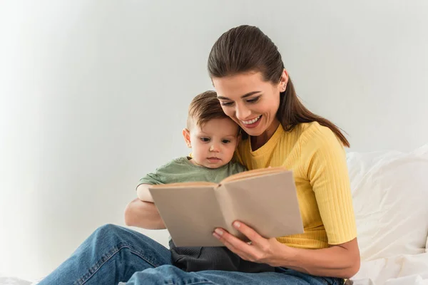 Sonriente Madre Leyendo Libro Borroso Cerca Niño Cama — Foto de Stock