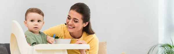 Junge Mutter Sieht Kleinkind Mit Löffel Der Nähe Von Essensschüssel — Stockfoto