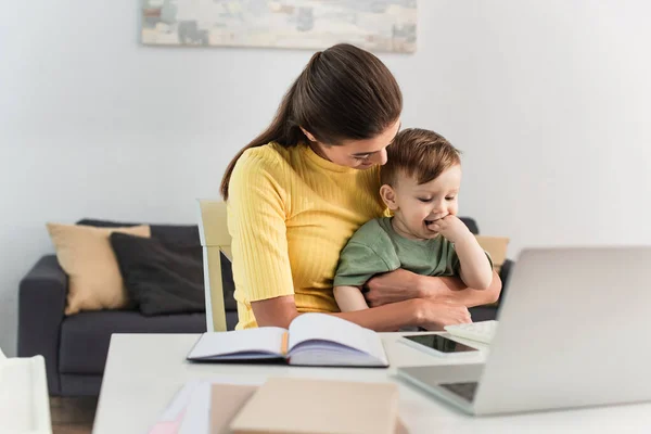 Young Mother Embracing Toddler Kid Gadgets Notebooks Blurred Foreground — Stock Photo, Image