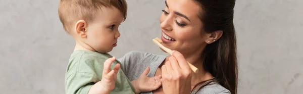 息子を見て歯ブラシを持つ若い母親 バナー — ストック写真