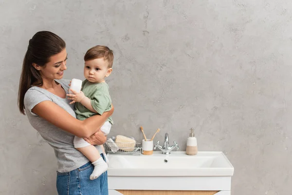 Smiling Woman Holding Kid Container Cream Bathroom — Stock Photo, Image