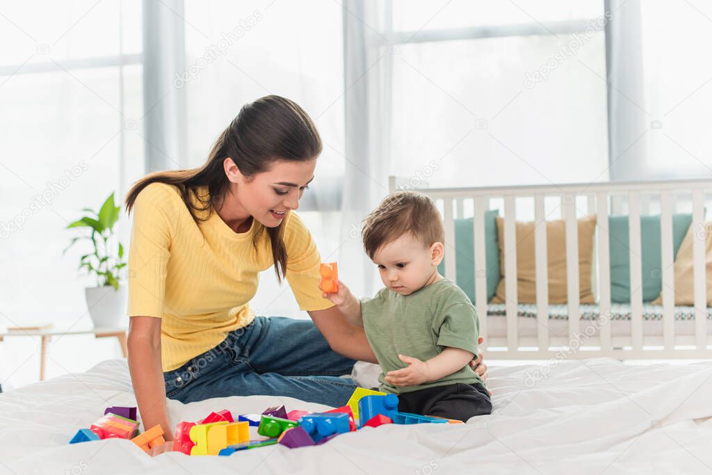 Positive mother and son playing colorful building blocks on bed 