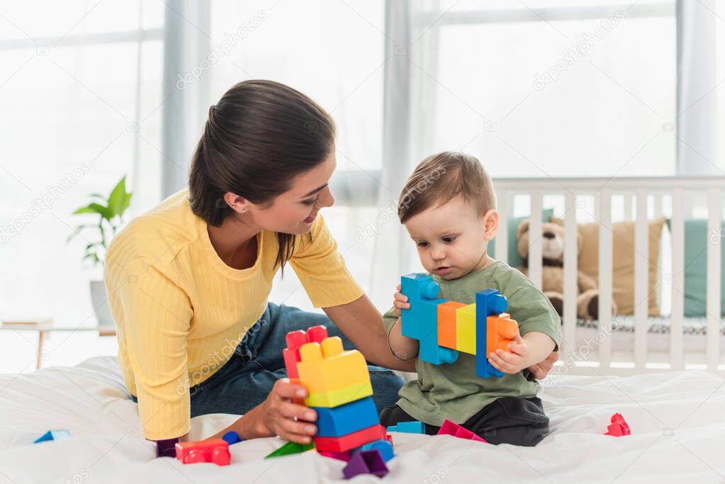 Young woman looking at child playing building blocks on bed 