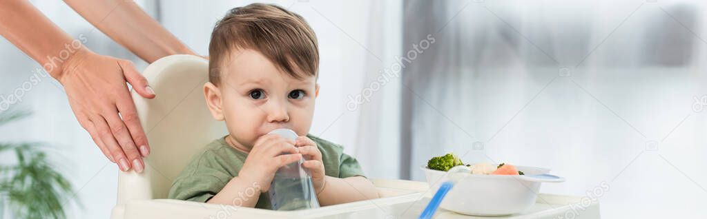 Mother holding high chair near toddler son with baby bottle and food, banner 