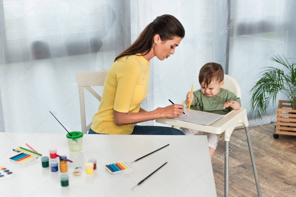 Woman drawing with son on high chair at home 