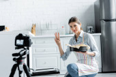 kulinářský blogger ukazující čas vaření při držení formy pečení v blízkosti rozmazaného digitálního fotoaparátu