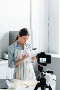Genç ev hanımı ham hamur yanında dijital tablet kullanıyor ve bulanık dijital kamera kullanıyor.