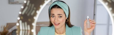 Şık bir güzellik blogcusu halka ışığı ve pankartın yanında bir şişe yüz serumu gösteriyor