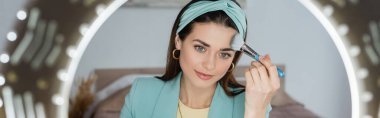 şık bir güzellik blogcusu halka ışığı ve pankartın yanında yüz pudrası uyguluyor