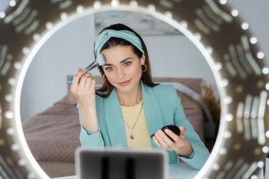 Bulanık akıllı telefon. Yanında daire ışığı var. Güzellik blogcusu yüz pudrası sürüyor.