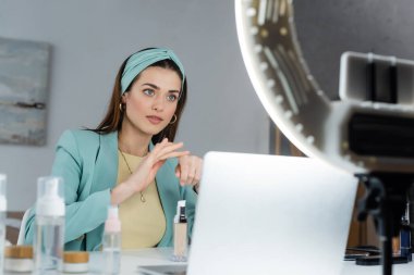 Bulanık dizüstü bilgisayar ve telefon kılıfının yanında yüz temeli uygulayan güzel bir kadın.