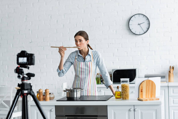 housewife tasting meal in front of blurred digital camera in kitchen