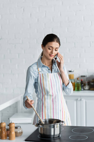 pretty housewife talking on mobile phone while preparing food in kitchen