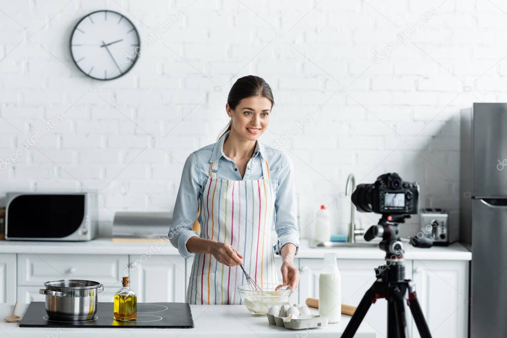 smiling woman preparing dough in front of digital camera in kitchen