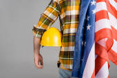 zpět pohled oříznutého dělníka s hardhatem a americkou vlajkou izolovaný na šedém, konceptu dne práce