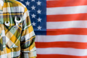 Teilansicht des Vorarbeiters mit Schraubenschlüssel in der Tasche des karierten Hemdes in der Nähe einer verschwommenen US-Flagge, Konzept des Arbeitstages
