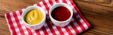 bowls with ketchup and mustard on checkered napkin and wooden table, banner clipart