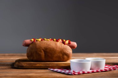 sauce bowls and plaid napkin near tasty hot dogs on wooden table isolated on grey clipart
