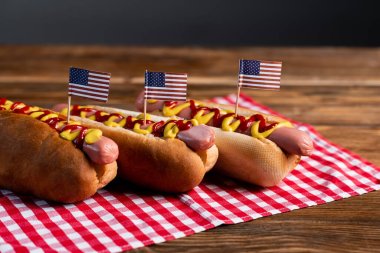 Küçük Amerikan bayraklı lezzetli sosisliler ve ahşap masa üzerindeki kareli peçeteler.