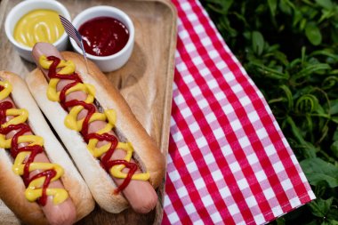 wooden tray with hot dogs, ketchup and mustard on table napkin and green grass clipart
