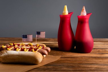 Küçük Amerikan bayraklı sosisli sandviçlerin yanındaki ayyaş şişeleri gri masalarda izole edilmiş ahşap masalarda.