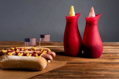 souse bottles near hot dogs with small american flags on wooden table isolated on grey clipart