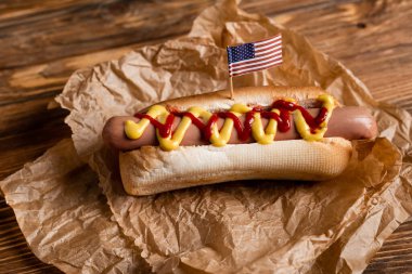 Küçük Amerikan bayrağı ve ahşap masadaki buruşuk parşömenli lezzetli sosisli sandviç.