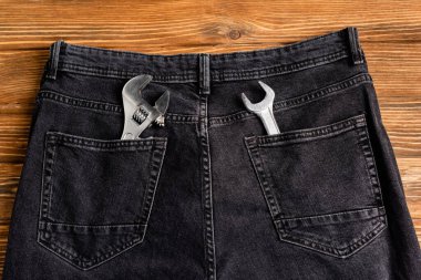 Arka ceplerinde İngiliz anahtarı olan kot pantolonların üst görünümü ahşap masa, işçi bayramı konsepti.