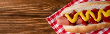 top view of tasty hot dog with sauces on checkered napkin and wooden table, banner clipart