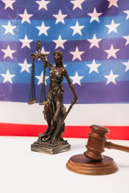 Tahta tokmak ve arka planda Amerikan bayrağı yakınında adalet heykeli. 