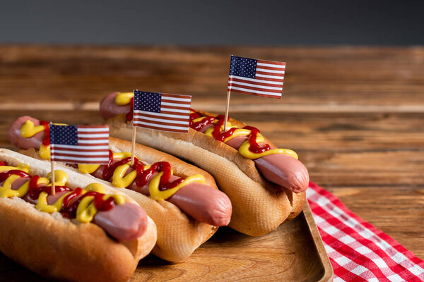 tasty hot dogs with sauces and small usa flags on wooden surface isolated on grey