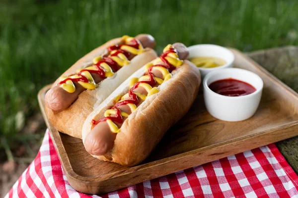 Holztablett Mit Saucenschalen Und Leckeren Hot Dogs Auf Karierter Tischserviette — Stockfoto