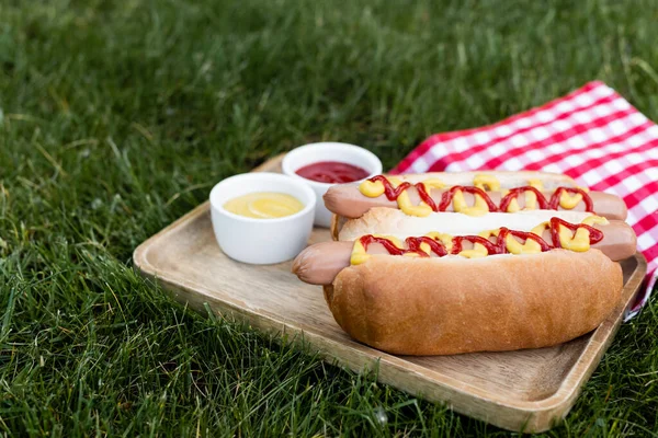 Holztablett Mit Saucenschüsseln Und Hot Dogs Neben Karierter Tischserviette Auf — Stockfoto