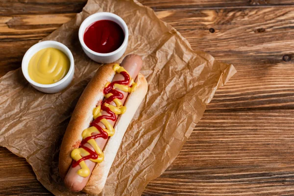 Pyszne Hot Dogi Pobliżu Miski Sosami Pognieciony Papier Kraft Drewnianym — Zdjęcie stockowe
