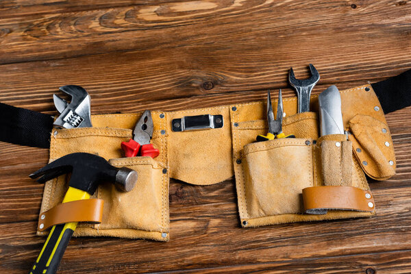 top view of leather tool belt with hammer, pliers, knife and wrenches on wooden table, labor day concept