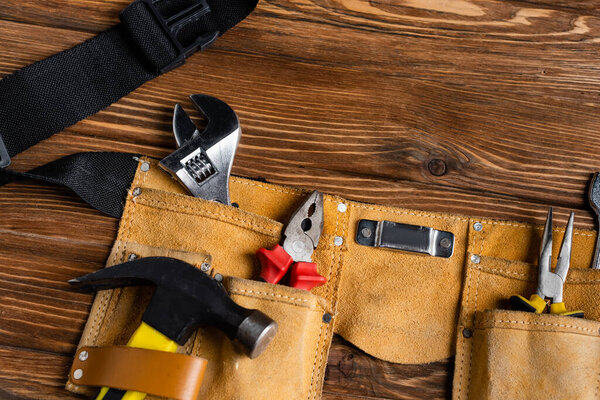 top view of leather tool belt with hammer, pliers and wrench on wooden table, labor day concept