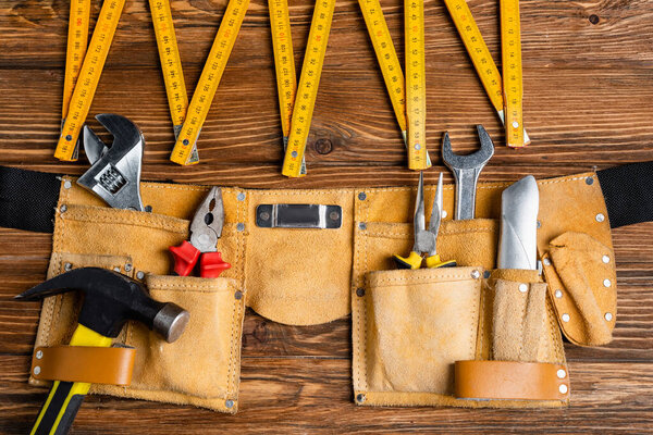top view of folding ruler and leather belt with various tools on wooden table, labor day concept
