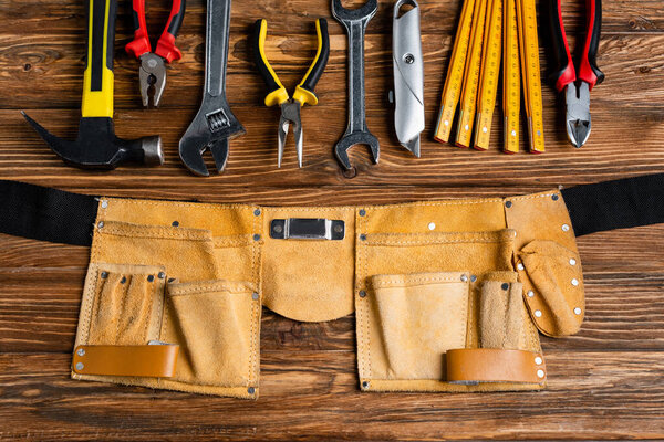 top view of various tools near leather tool belt on wooden table, labor day concept