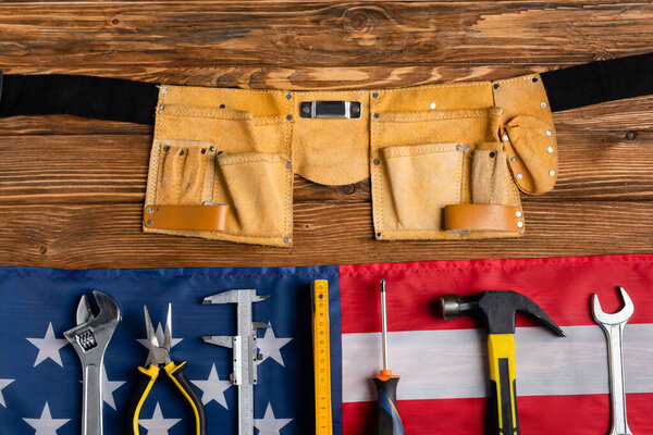 top view of leather tool belt, usa flag and various tools on wooden table, labor day concept