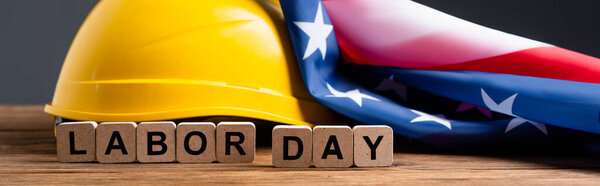 cubes with labor day lettering near helmet and usa flag on wooden surface isolated on grey, banner