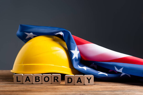 cubes with labor day lettering near hardhat and usa flag on wooden surface isolated on grey