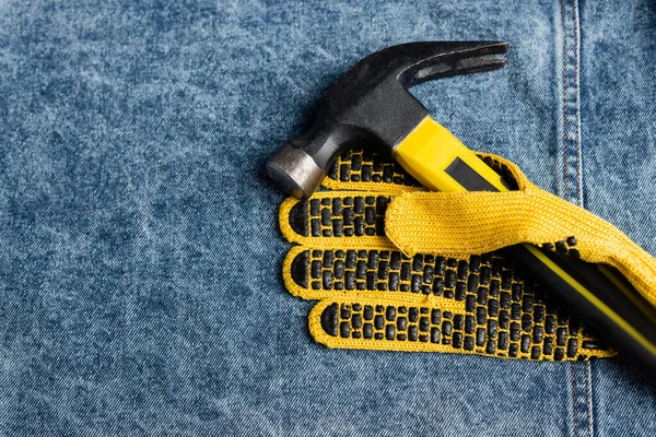 top view of yellow work gloves and hammer on blue denim cloth, labor day concept