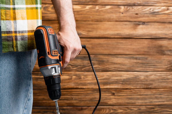 partial view of builder with electric drill near wooden wall, labor day concept