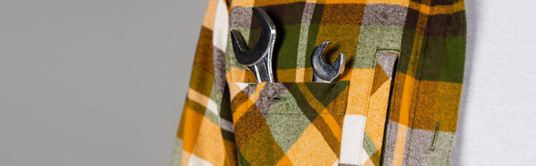 partial view of handyman with wrenches in pocket of plaid shirt isolated on grey, labor day concept, banner