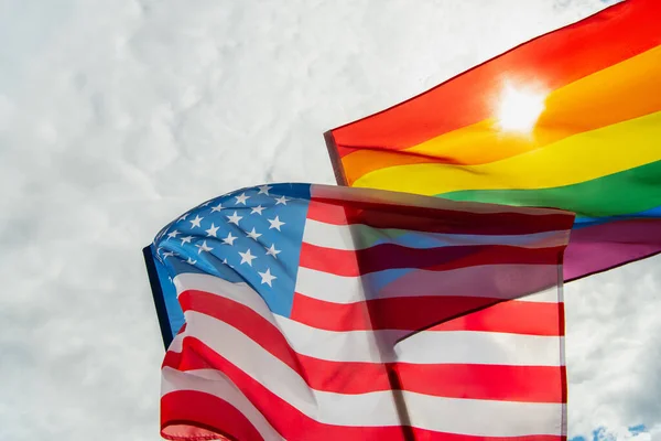low angle view of american and colorful lgbt flags against sky 