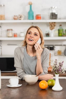 Mutfakta cep telefonuyla konuşan mutlu bir kadın. 